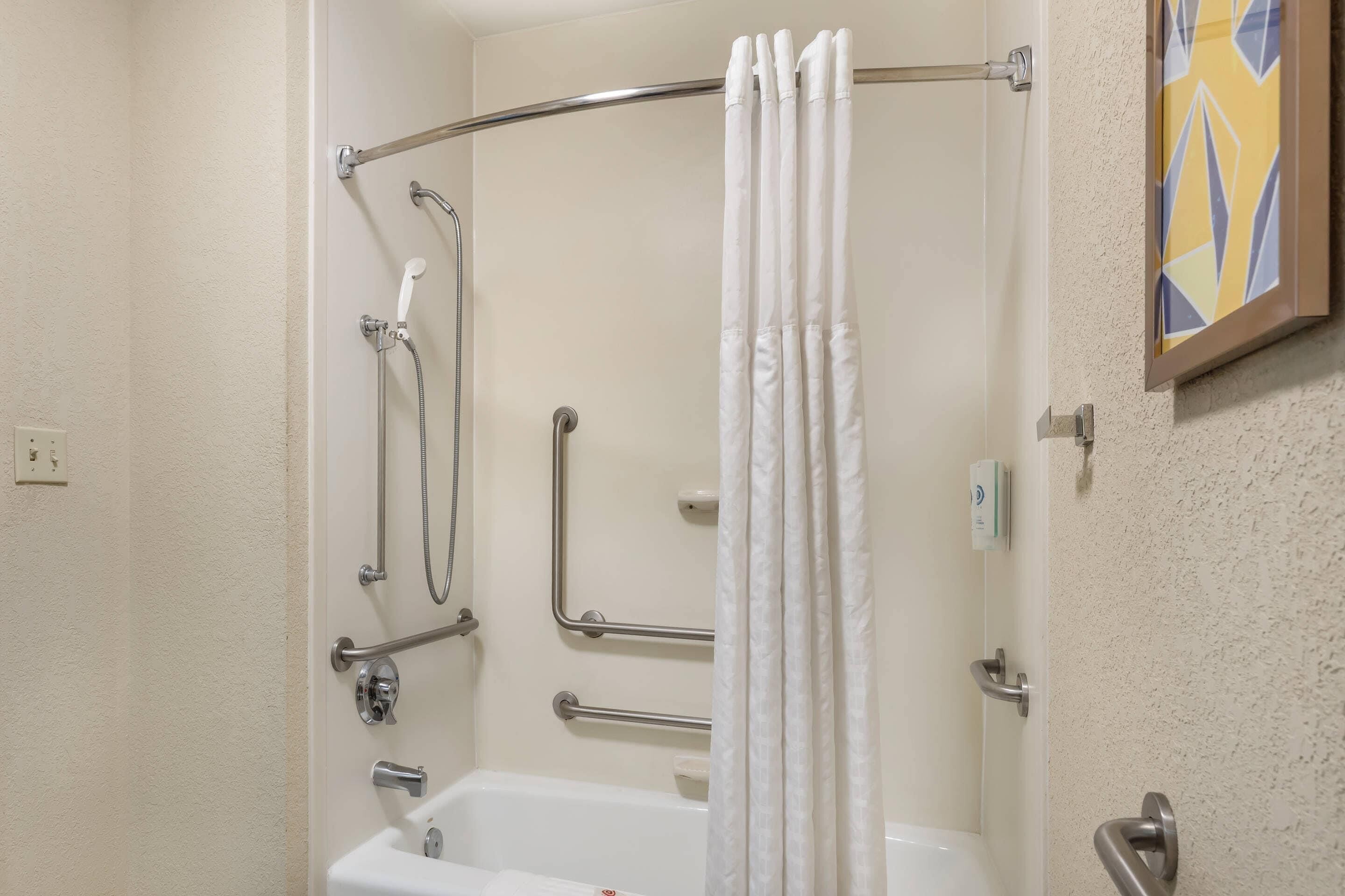 A shower with a white curtain, grab bars, and a handheld showerhead.