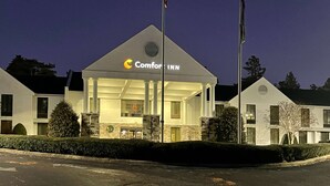 A Comfort Inn hotel with a prominent sign, a flagpole, and a well-lit entrance.