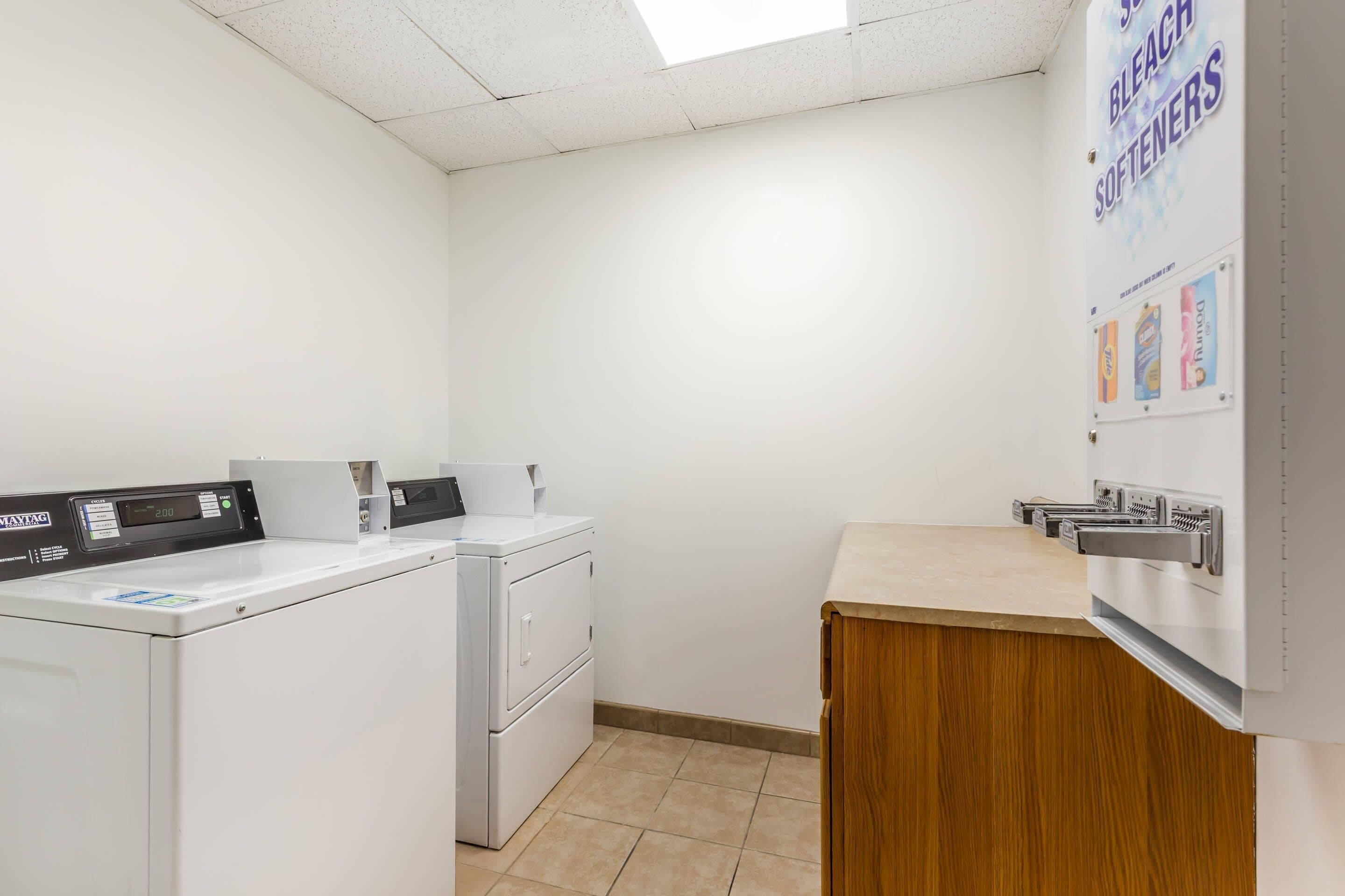 A laundry room with a washing machine, dryer, and a bulletin board with bleach softeners.