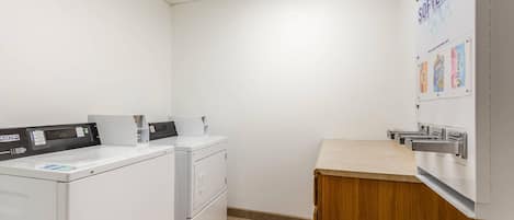 A laundry room with a washing machine, dryer, and a bulletin board with bleach softeners.