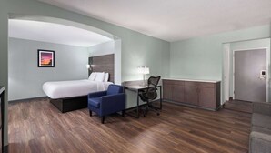 A hotel room with a bed, a desk with a chair, a small sofa, and a door. - Baymont by Wyndham Creedmoor (Creedmoor)