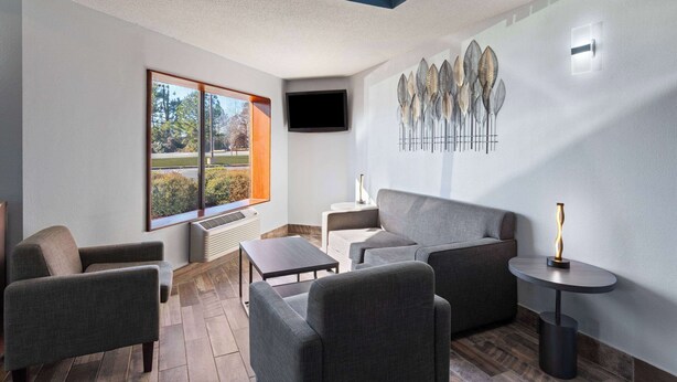 A modern lounge area with a sofa, armchairs, a small table, and a decorative wall piece. - Baymont by Wyndham Creedmoor (Creedmoor)