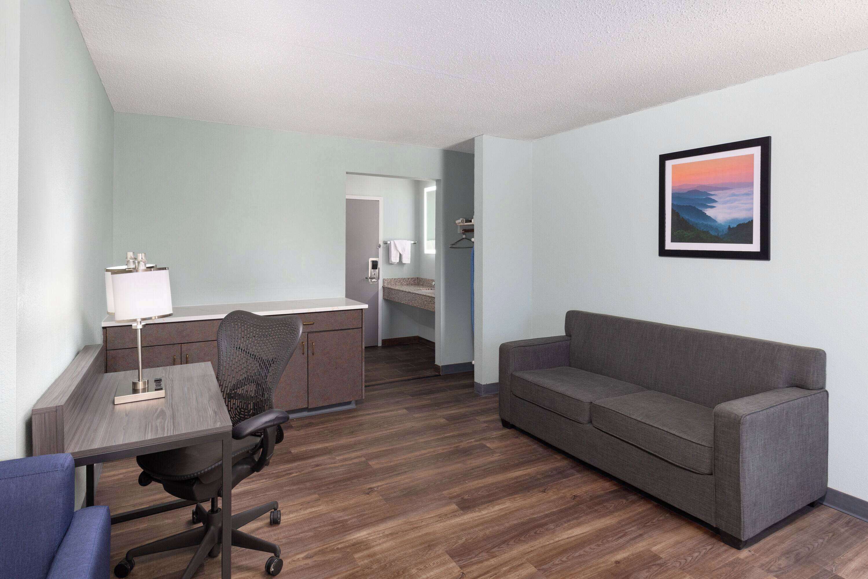 Een moderne hotelkamer met een houten vloer, een grijze bank, een bureau met een lamp en een lijst met een afbeelding aan de muur.