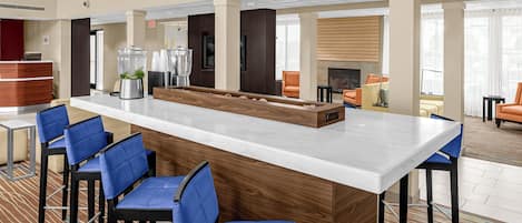 Un área de bar moderna con una isla central, taburetes de bar azules y un mostrador de recepción.