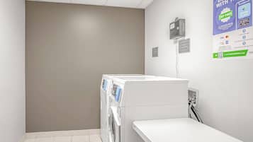 Una sala de lavandería con lavadora, secadora y un letrero que indica que hay productos de lavandería disponibles en la recepción.