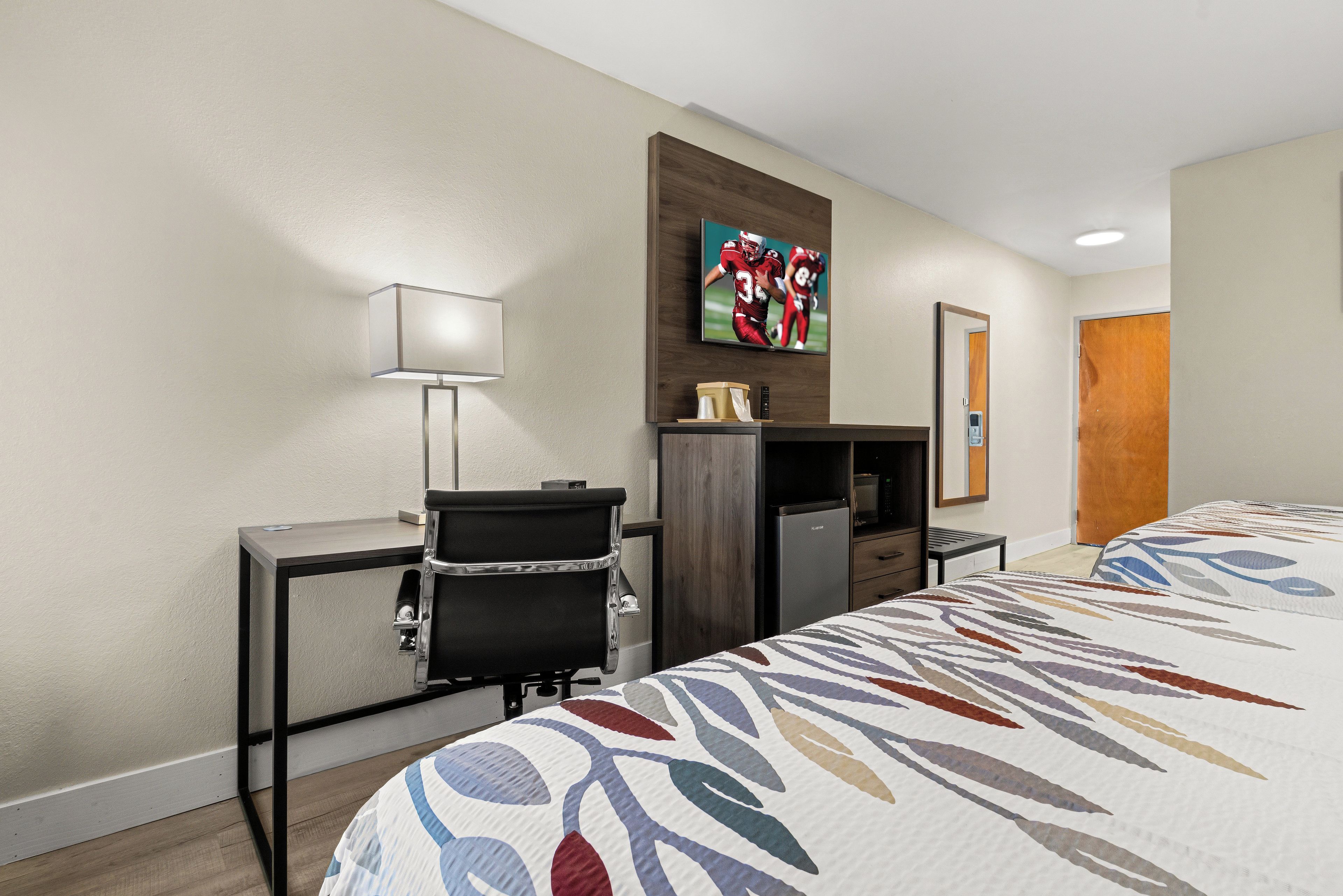A hotel room with two beds, a desk, a chair, a television, and a microwave.