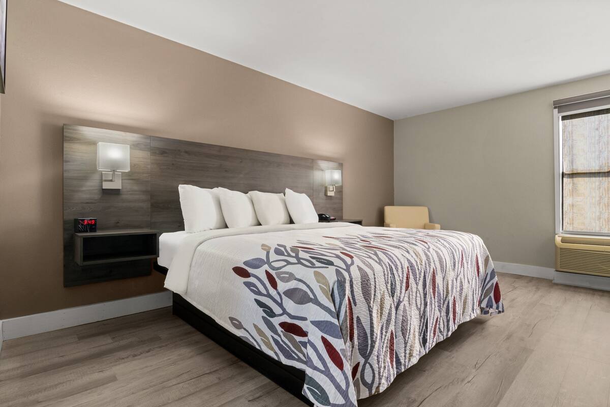 A modern bedroom with a large bed, built-in nightstands, wall-mounted lights, and a window with blinds.