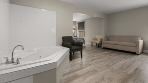 A modern living room with a large white bathtub, a dark armchair, a beige sofa, and a wooden floor. - Red Roof Inn Washington, NC (Washington)