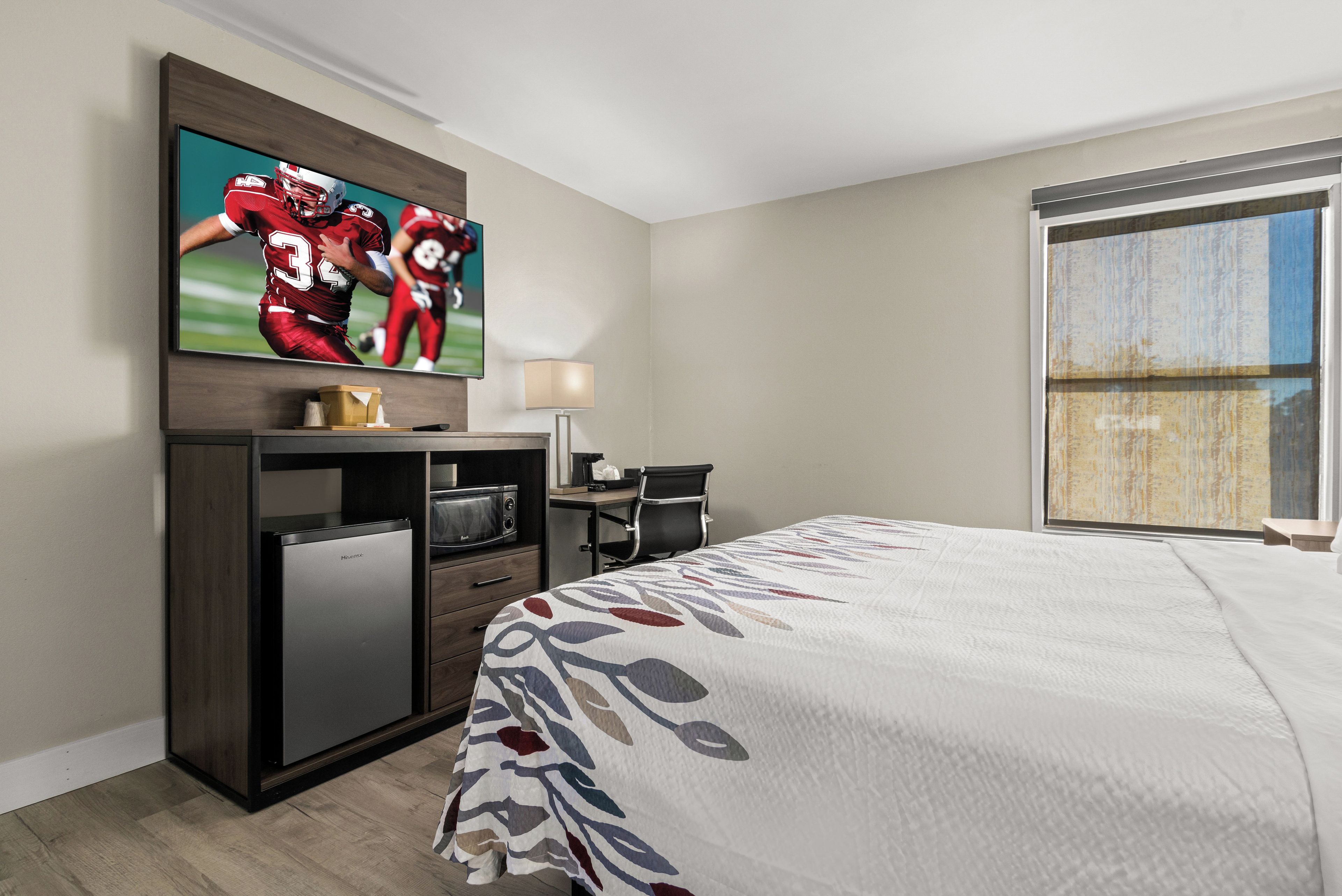 Habitación de hotel con cama, escritorio, televisor montado en la pared y ventana.