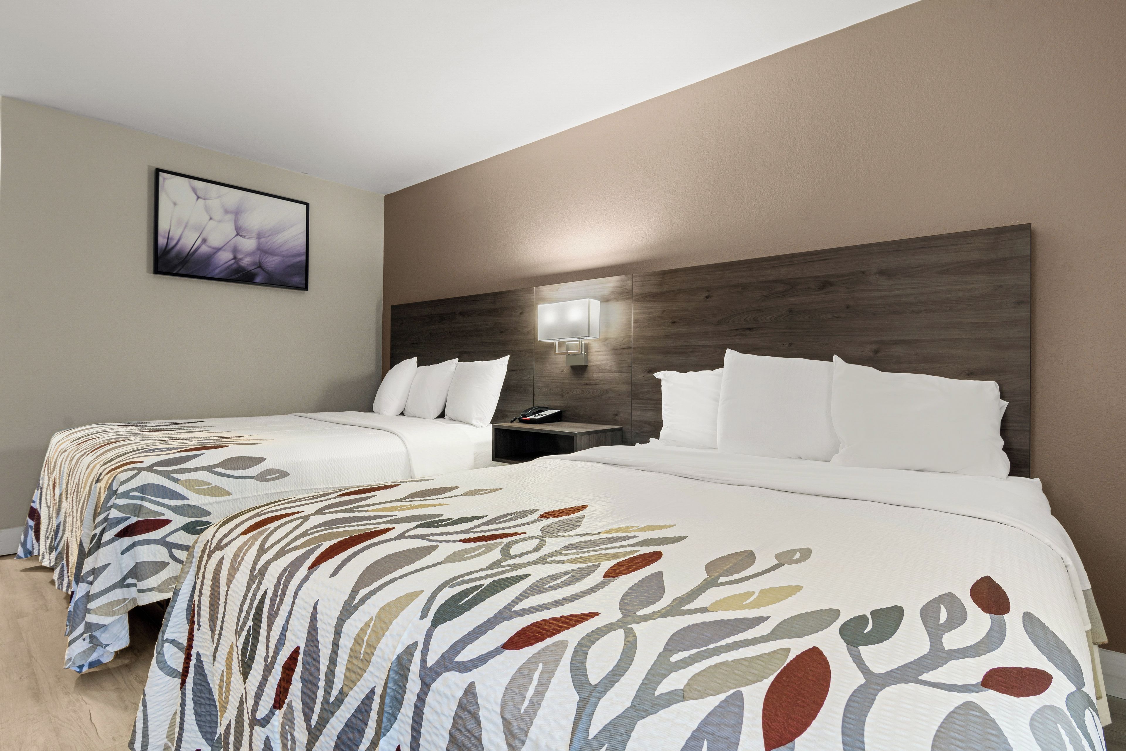 Ein Hotelzimmer mit zwei Betten, einem Nachttisch, einer Wandlampe und einem gerahmten Bild.