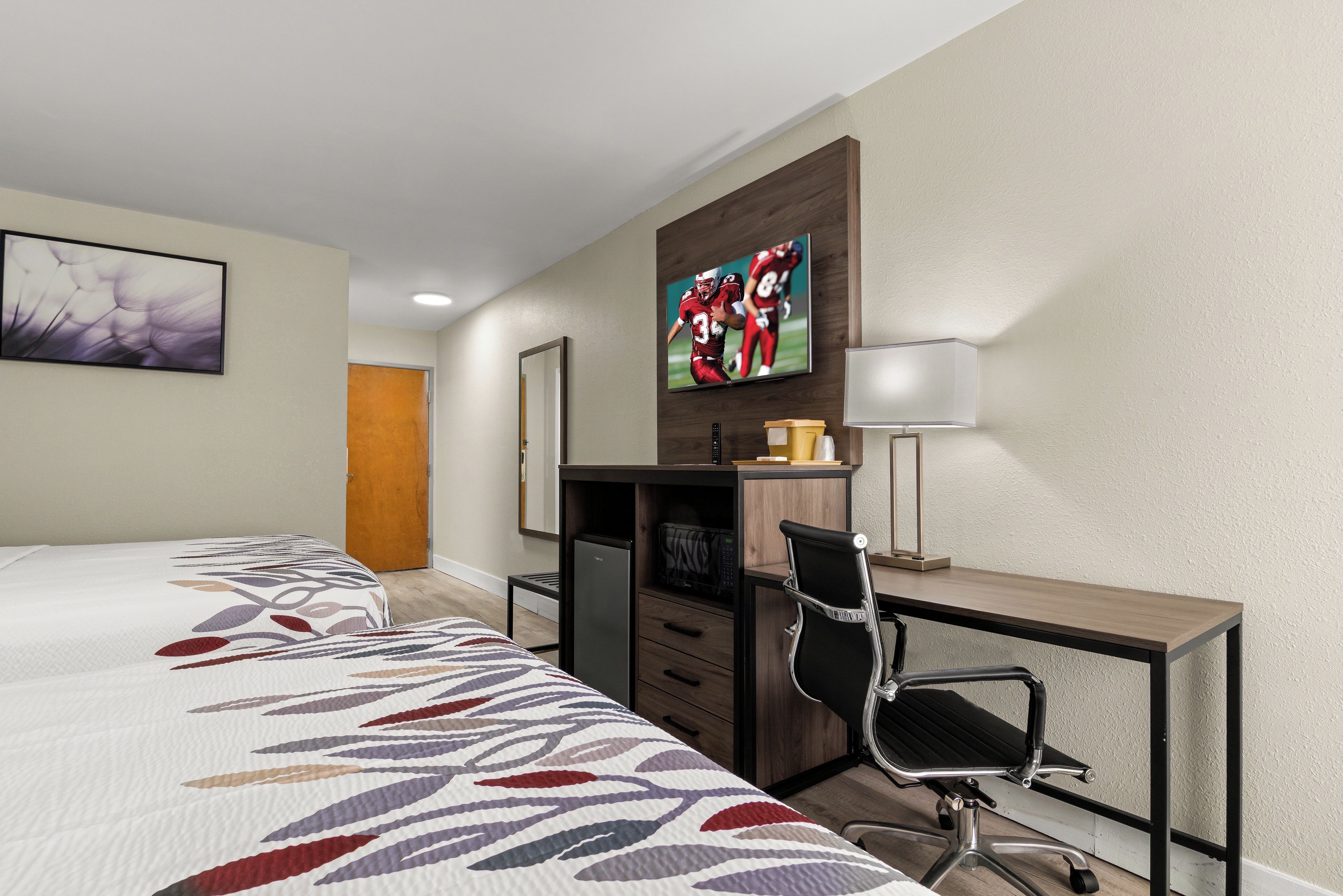 A hotel room with a bed, a desk with a chair, a television, and a lamp.