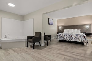 Un dormitorio moderno con una cama grande, un rincón de descanso con dos sillones, un baño con bañera y una lámpara en el techo.