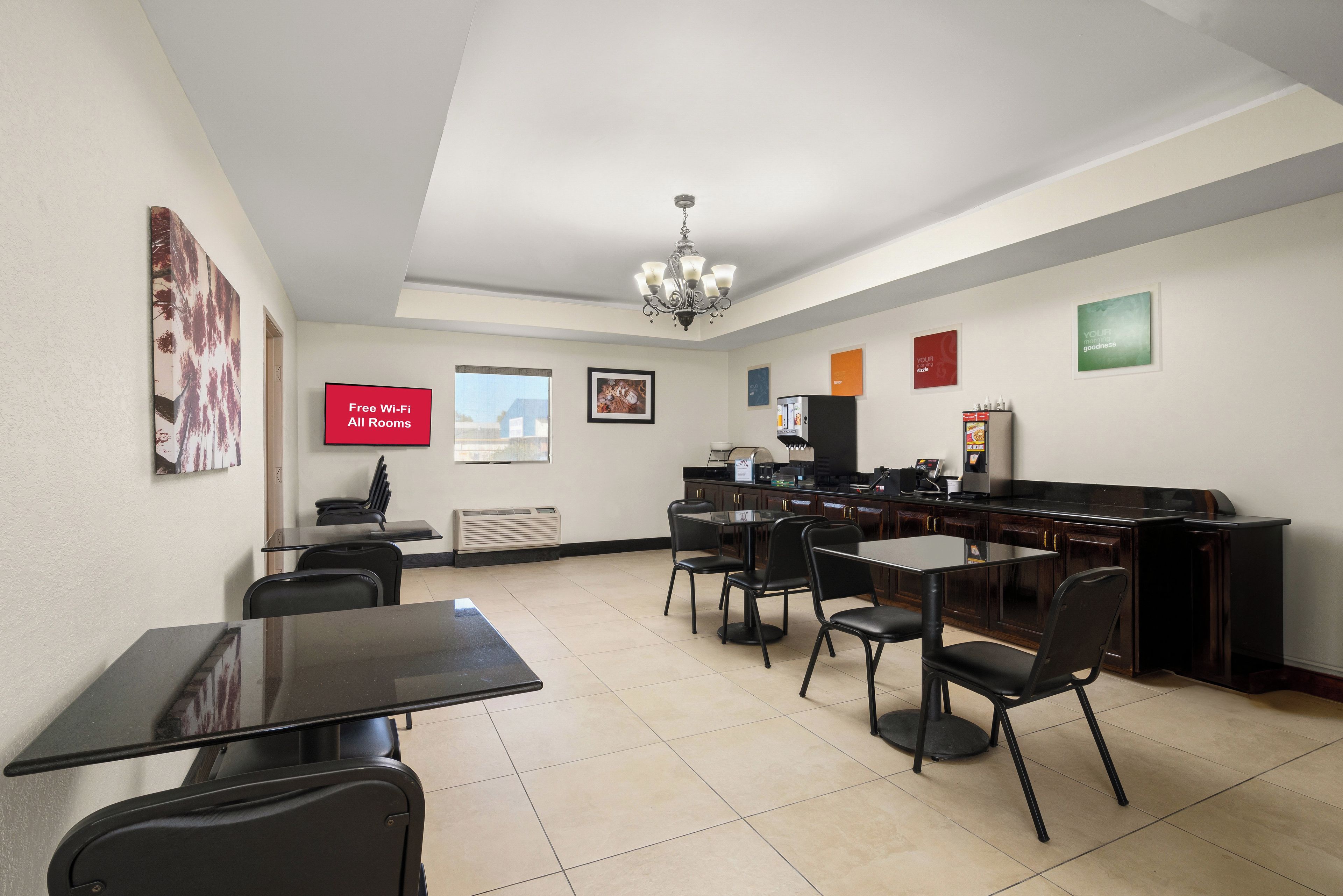 A hotel room with a dining area, a TV displaying 'Free Wi-Fi All Rooms,' a coffee machine, and a refrigerator.