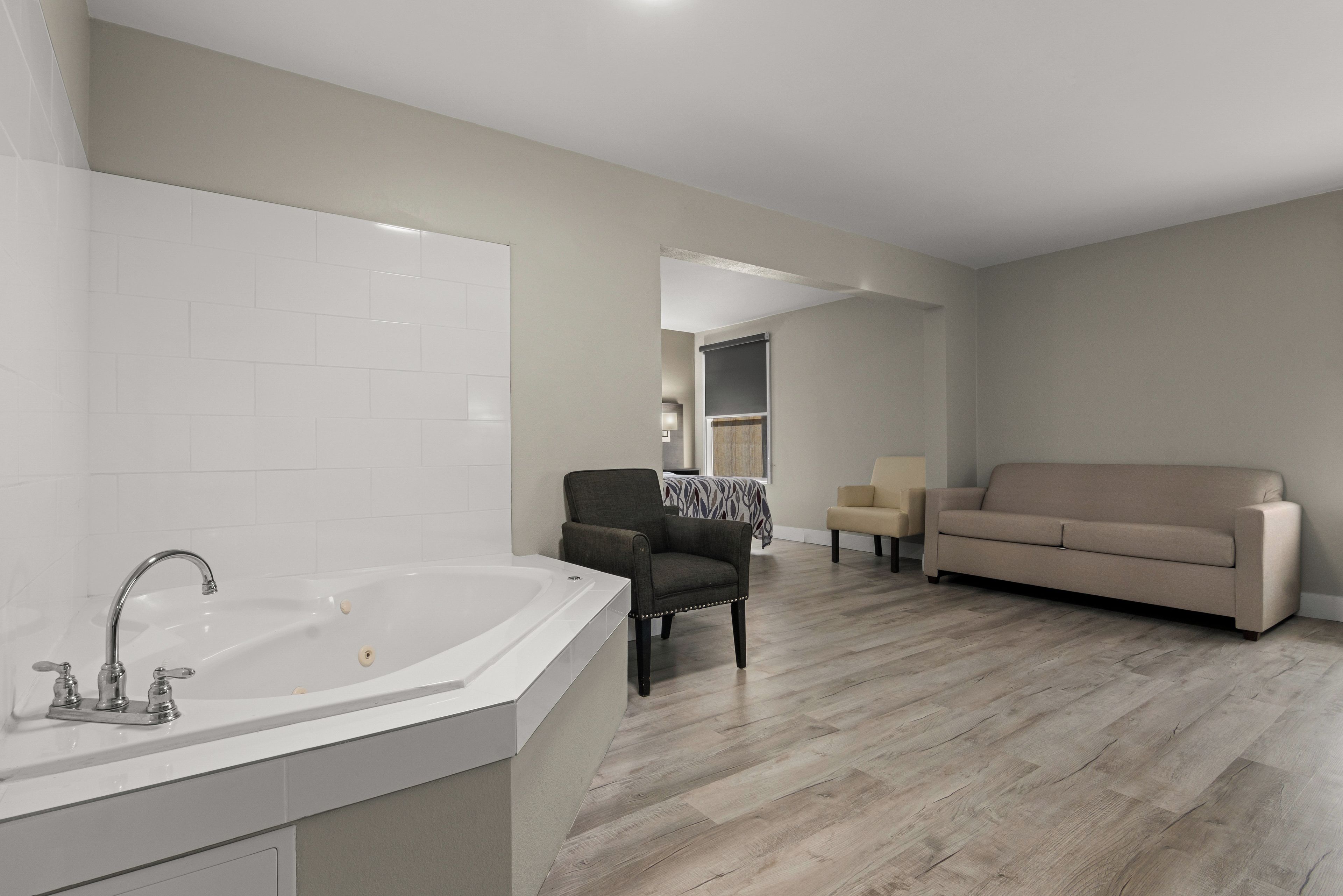 A modern living room with a large white bathtub, a dark armchair, a beige sofa, and a dining area in the background.