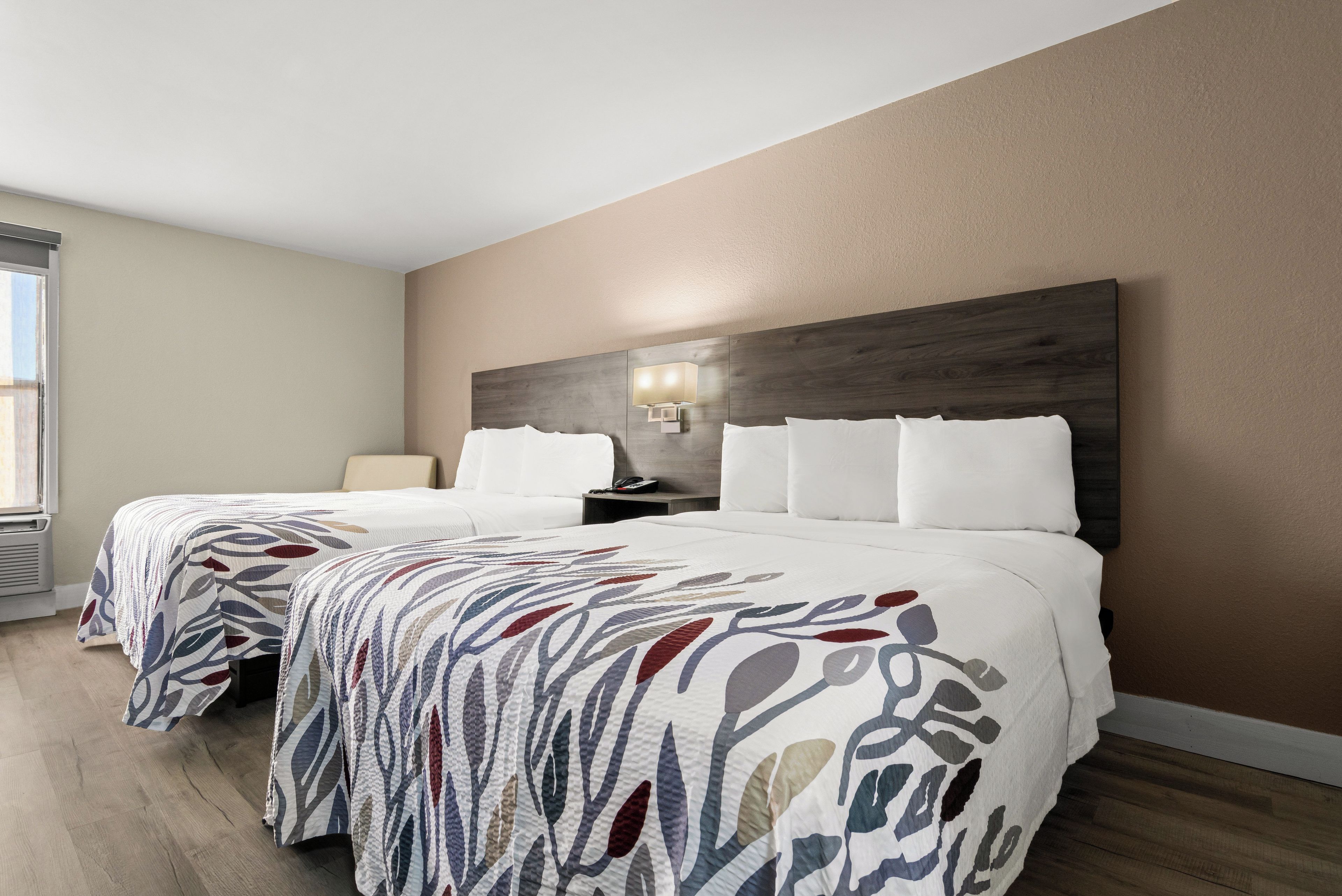 A hotel room with two beds, a nightstand, a lamp, and a window.