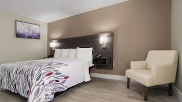 A hotel room with a bed, bedside table, lamp, chair, and a wall-mounted phone.