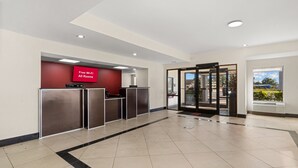 A hotel reception area with a red wall, a digital display advertising free Wi-Fi, and a revolving door. - Red Roof Inn Washington, NC (Washington)