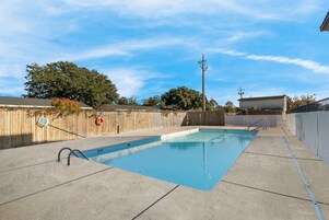 Una piscina rectangular con plataforma de hormigón, rodeada por una valla de madera y árboles.