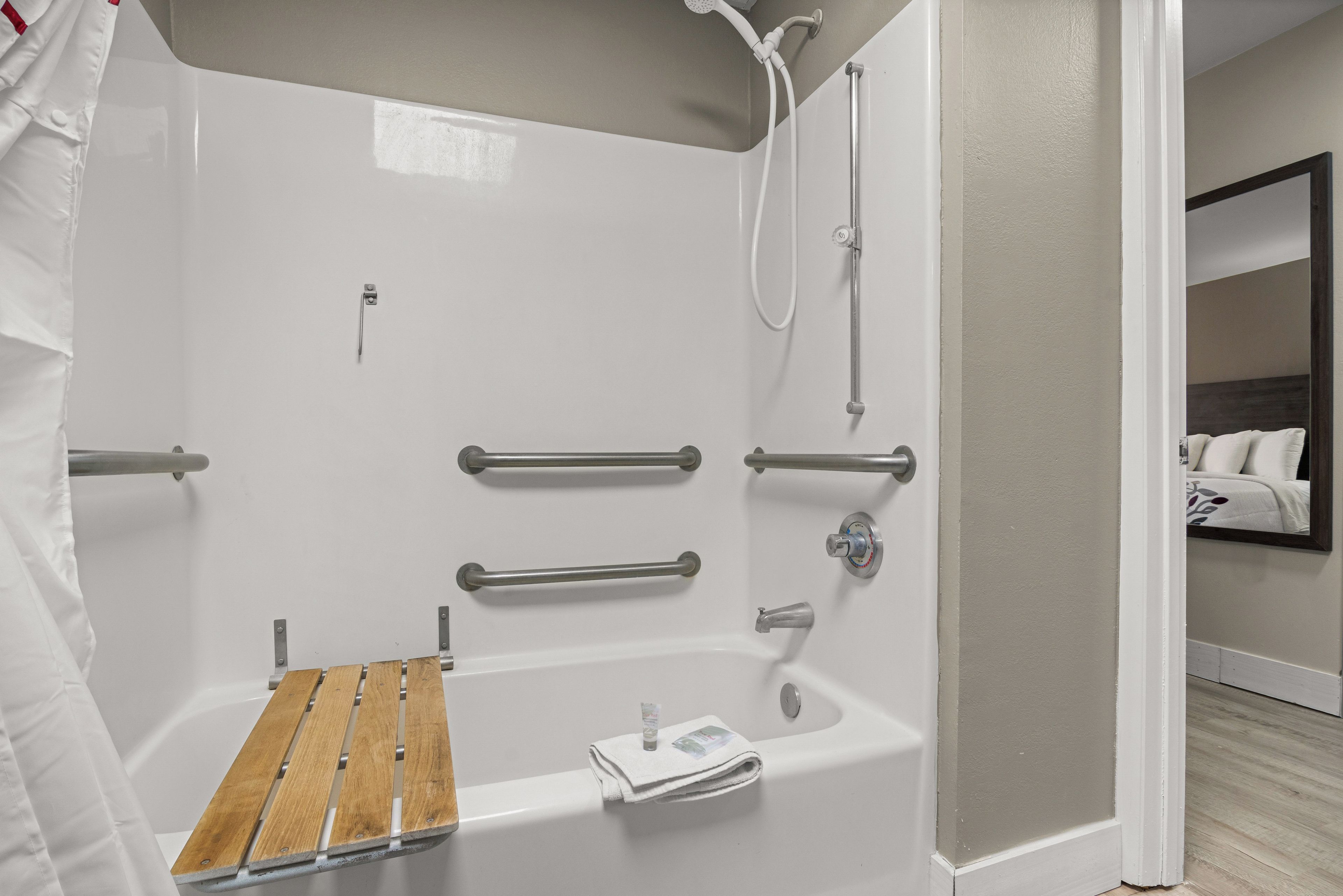 Ein modernes Badezimmer mit einer barrierefreien Dusche, Haltegriffen, einer Holzbadematte und einem Handtuchhalter.