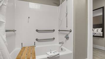 Ein modernes Badezimmer mit einer barrierefreien Dusche, Haltegriffen, einer Holzbadematte und einem Handtuchhalter.