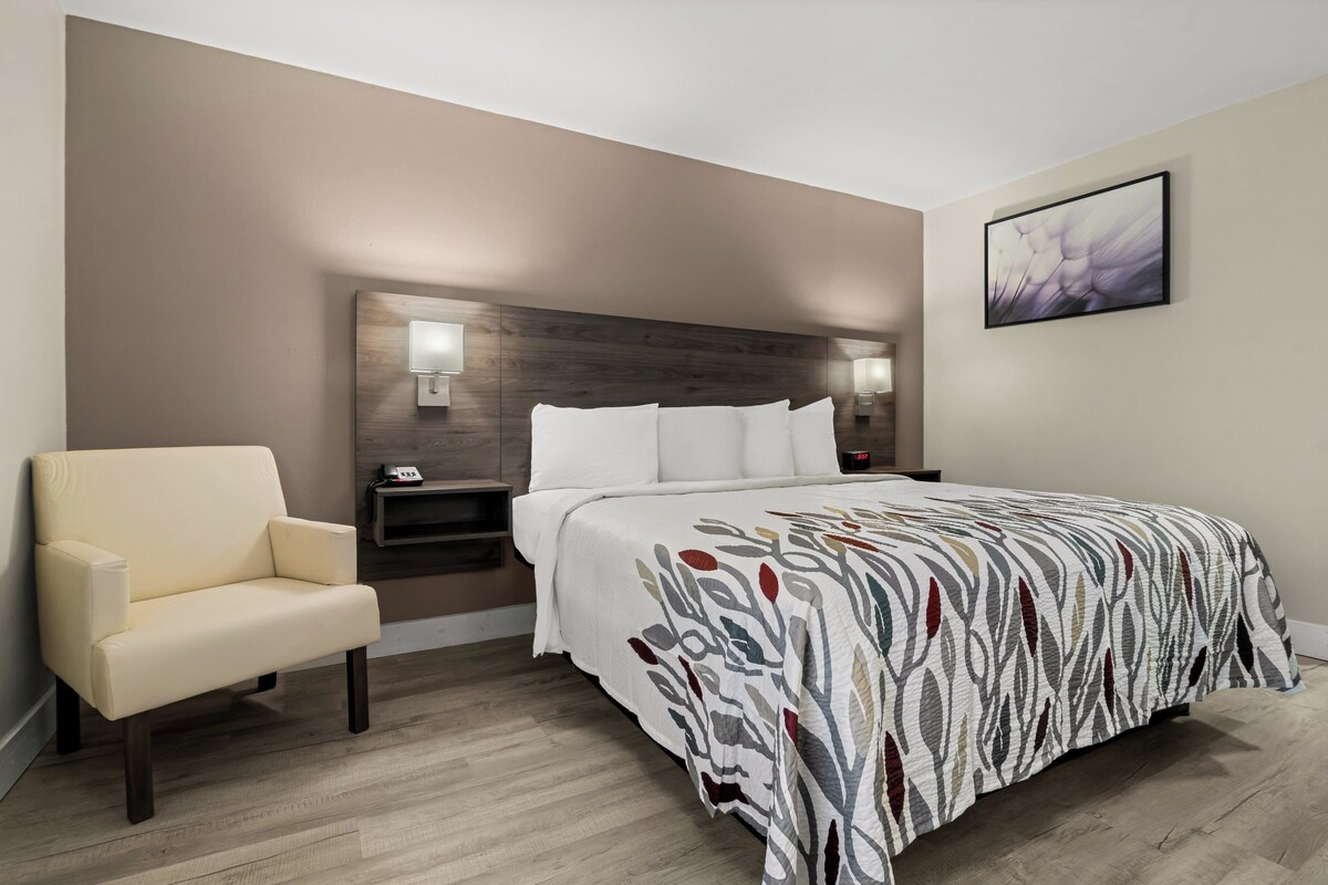 A hotel room with a bed, a chair, a nightstand, and a wall-mounted lamp.