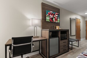 Quarto de hotel com escrivaninha, cadeira, televisão e micro-ondas.