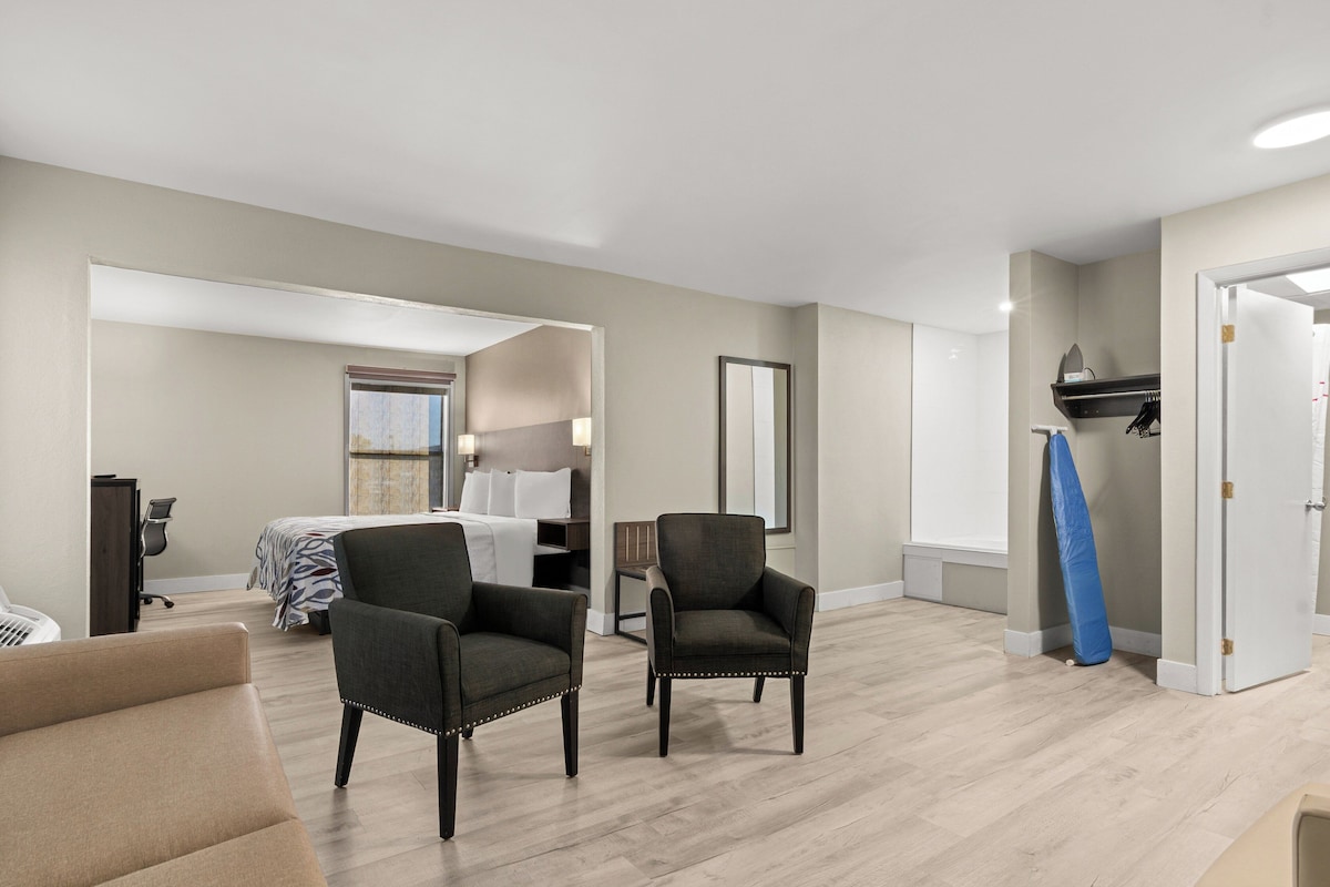 A hotel room with a bed, two armchairs, a desk, and a mirror.