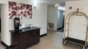 A hotel lobby with a coffee station, artwork on the wall, and a luggage cart. - Red Roof Inn Washington, NC (Washington)