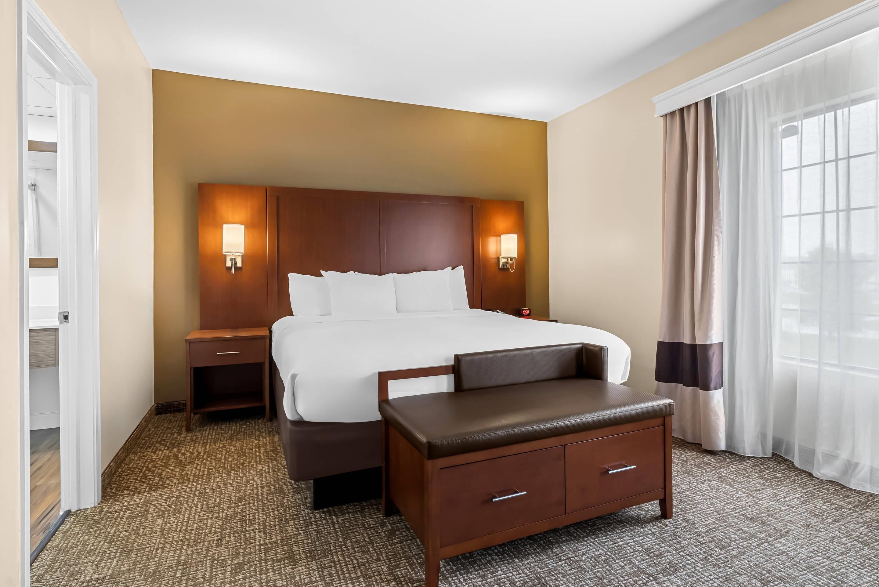 Une chambre d’hôtel avec un grand lit, une table de chevet, une commode, un bureau et une chaise.