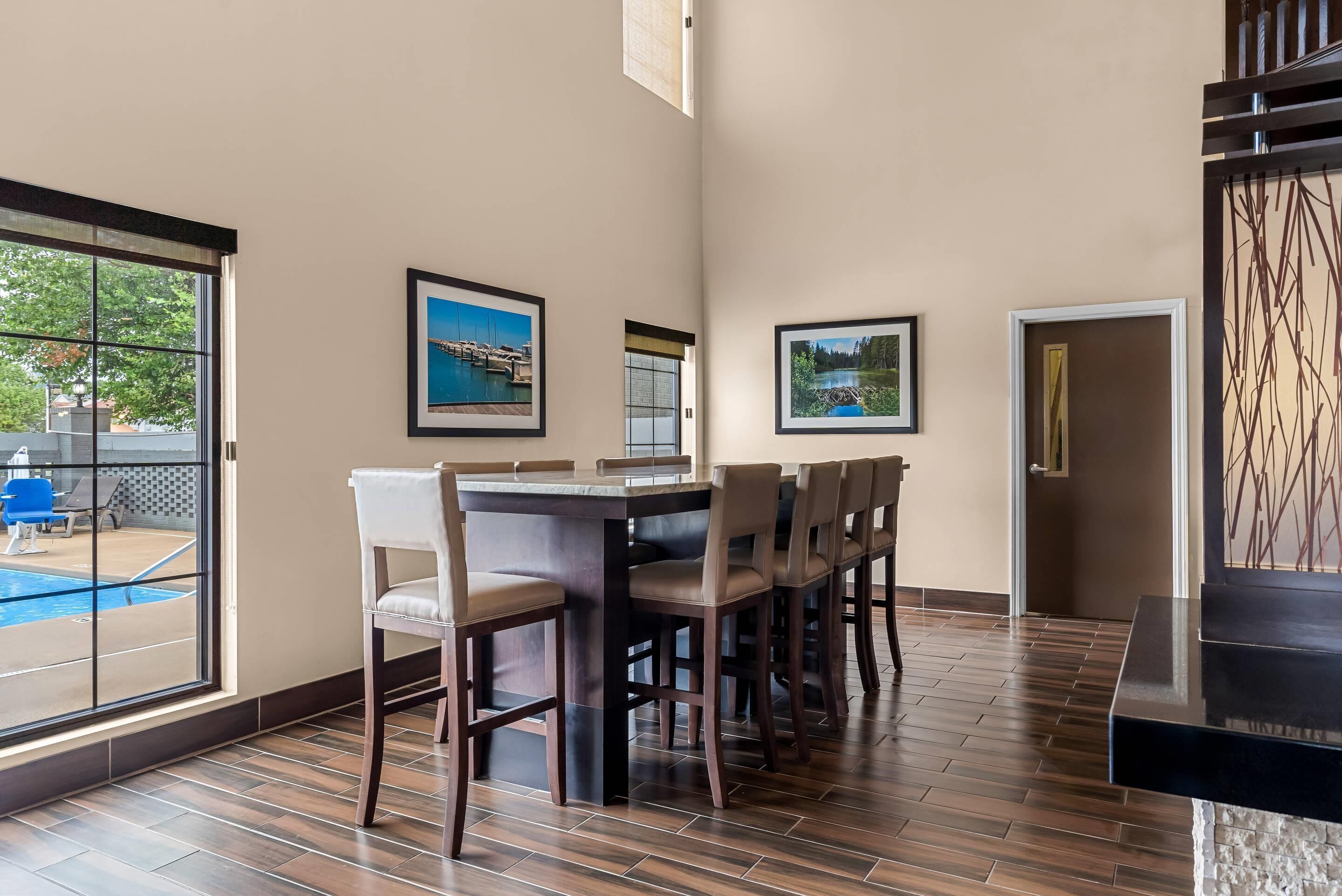 Un comedor con una mesa y sillas de madera, vista a la piscina y cuadros en la pared.