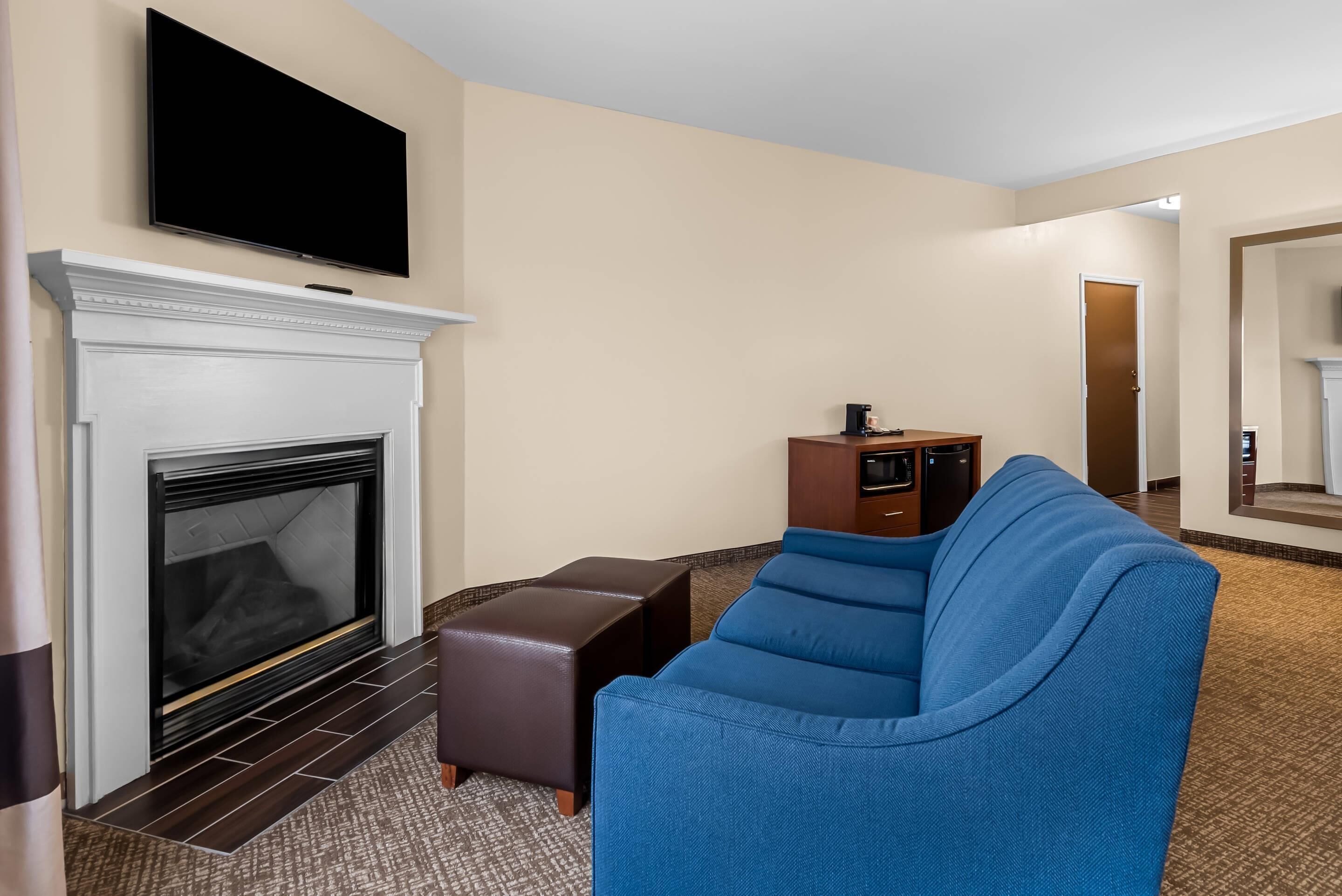 Une chambre d’hôtel avec une cheminée, un téléviseur à écran plat fixé au-dessus, un canapé bleu et une petite armoire en bois.