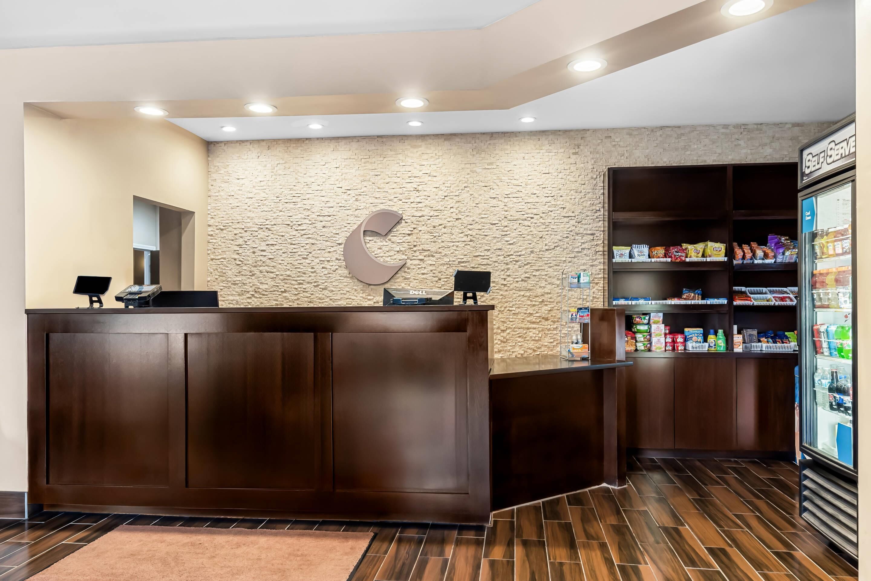 Un espace d’accueil comprenant un comptoir de réception en bois, un mur à l’aspect pierre, un distributeur automatique de boissons en libre-service et une étagère à collations.