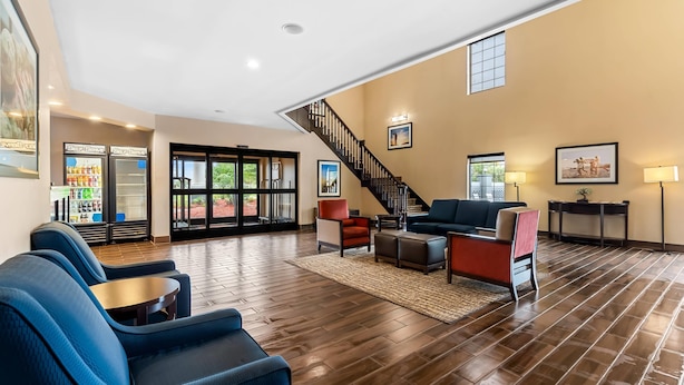 A spacious lobby with a wooden floor, blue seating, a staircase, and a bar area with refrigerators. - Comfort Suites near Camp Lejeune (Jacksonville)