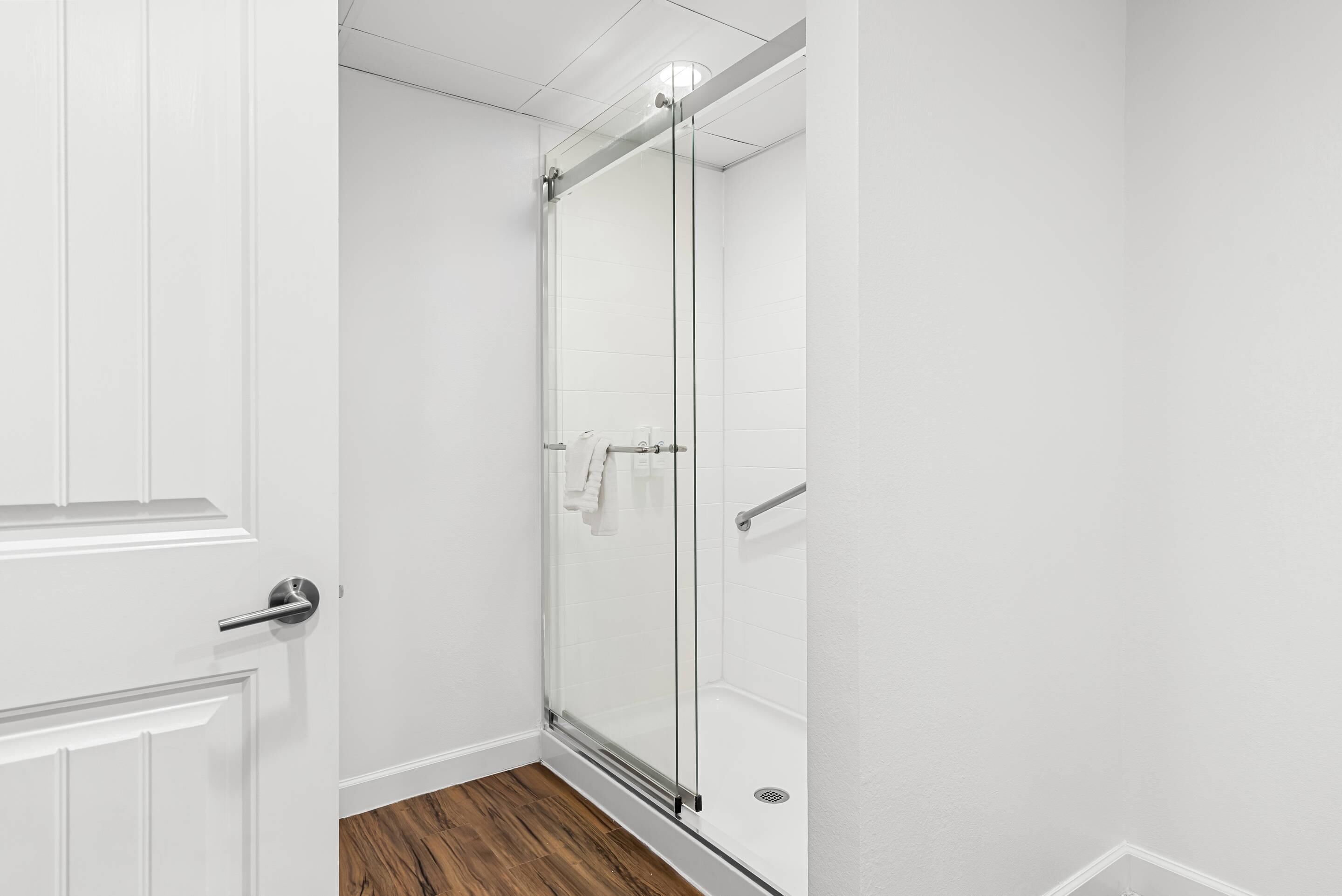 Un baño moderno con cabina de ducha de vidrio, paredes blancas y suelo de madera.