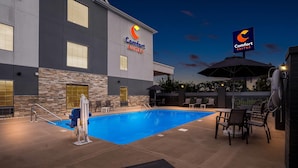 A Comfort Suites hotel with a swimming pool, outdoor seating, and a stone facade. - Comfort Suites near Camp Lejeune (Jacksonville)