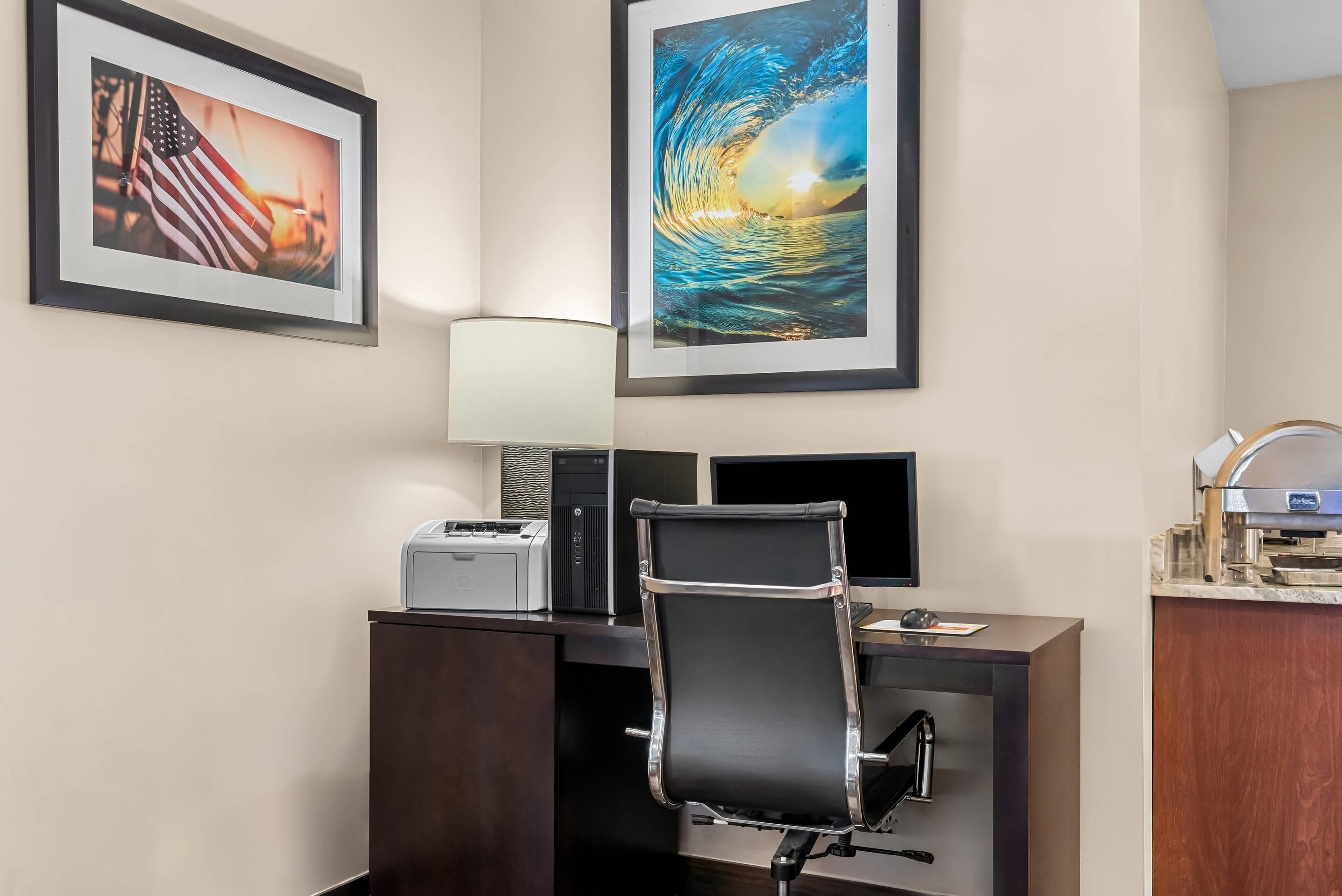 Un bureau d’hôtel équipé d’un bureau, d’écrans d’ordinateur, d’une imprimante et de tableaux représentant le drapeau américain et une vague.