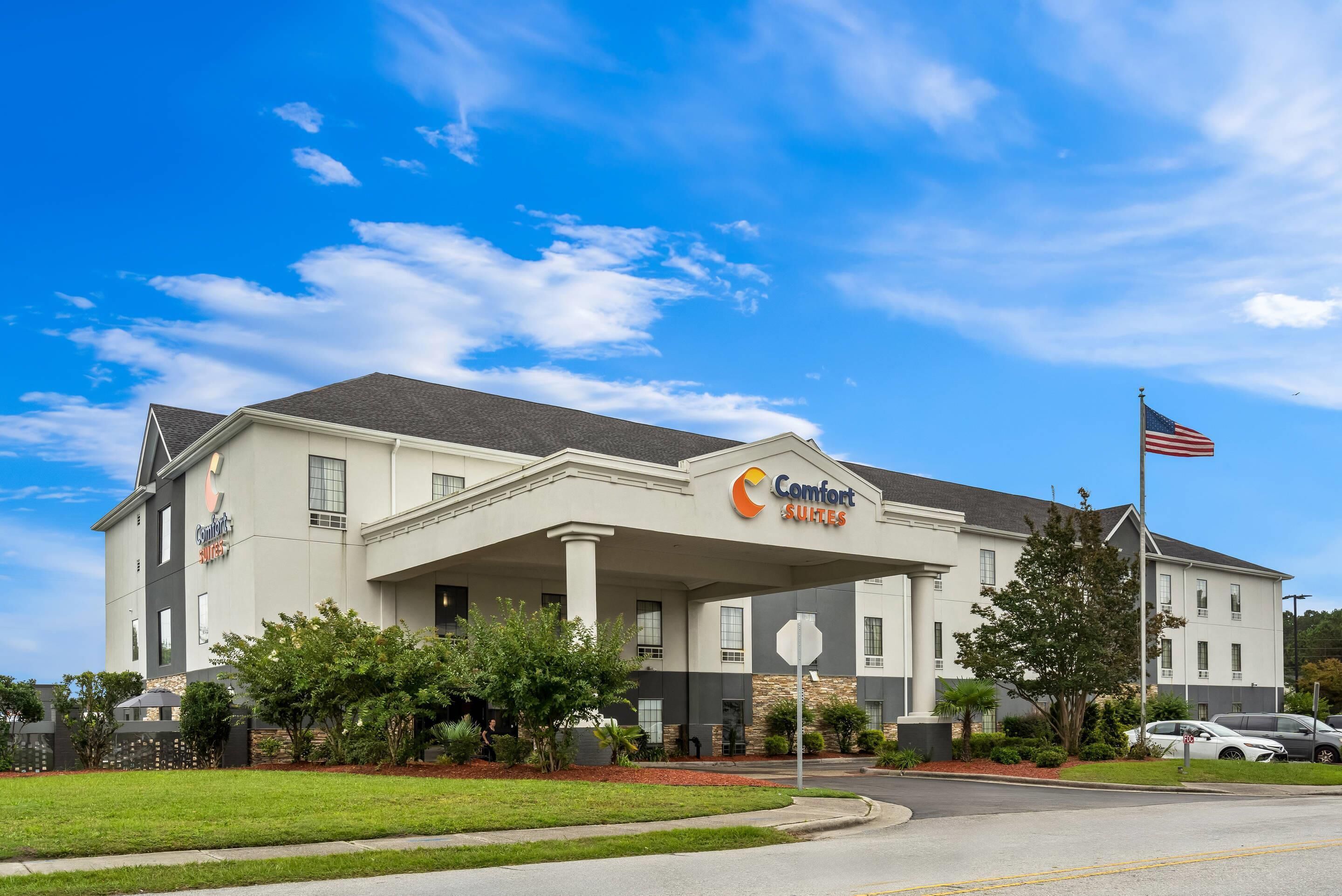 Un hotel Comfort Suites con una entrada amplia, una bandera y un césped bien cuidado.