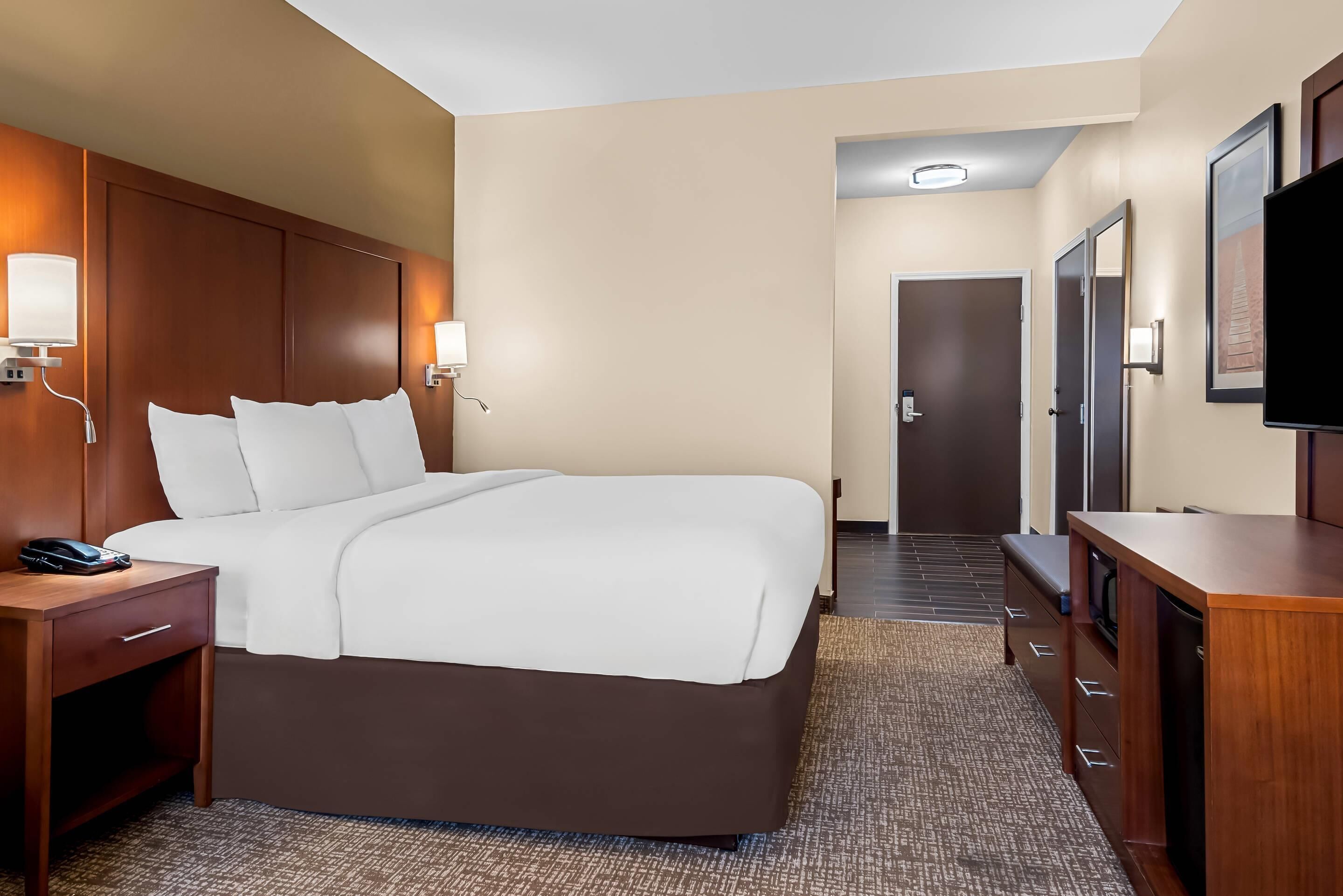 A hotel room with a large bed, bedside tables, a desk, and a television.