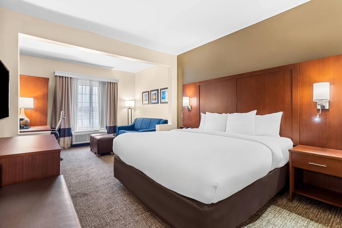 Ein Hotelzimmer mit einem großen Bett, einem Schreibtisch, einem Sessel und einem Fernseher.