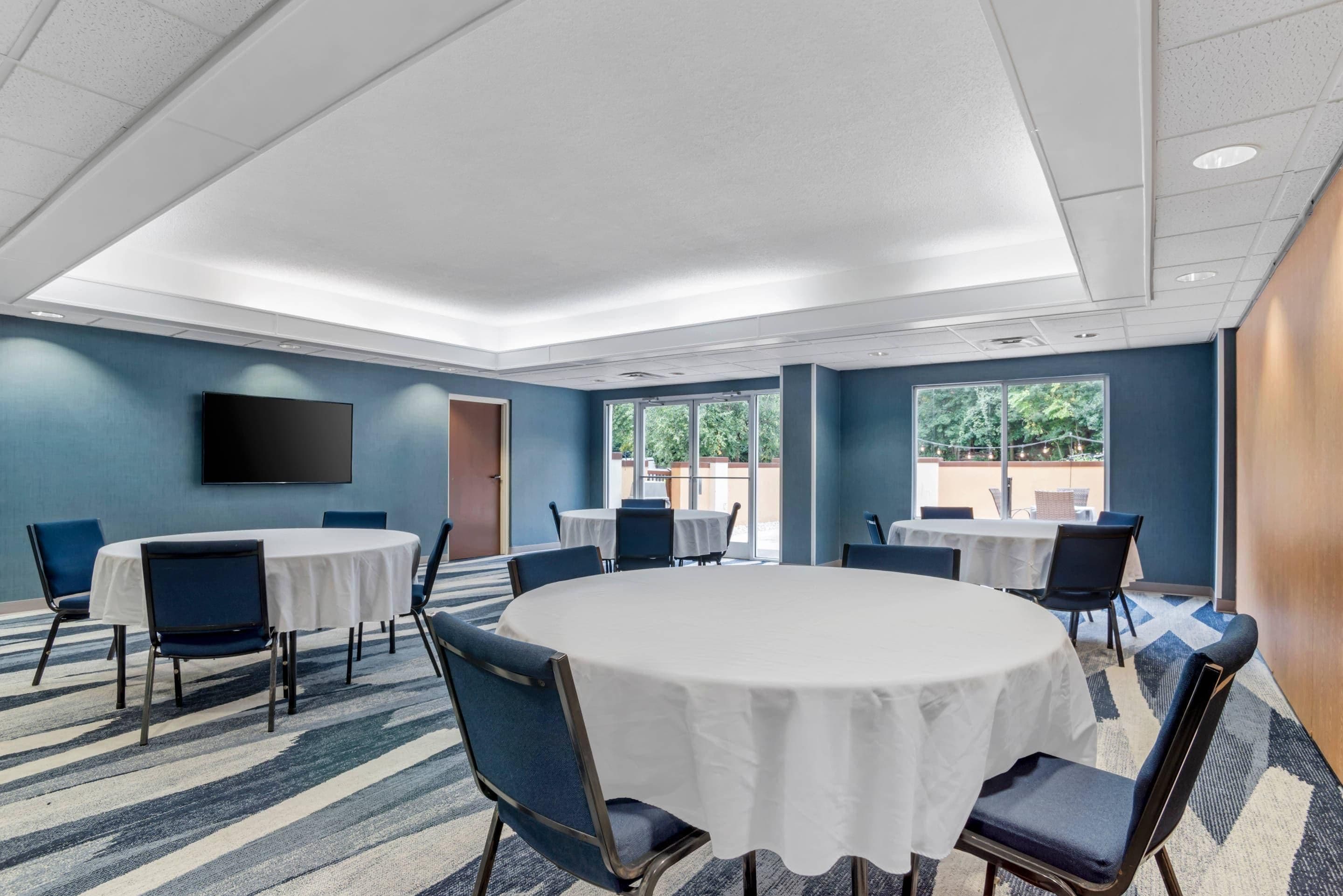 Une salle de conférence équipée de tables rondes, de chaises, d’un téléviseur à écran plat et de grandes fenêtres.