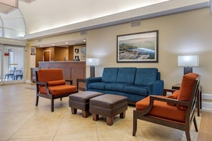 A lobby with a reception desk, blue sofa, orange armchairs, and a painting on the wall. - Comfort Suites Gastonia - Charlotte (Gastonia)