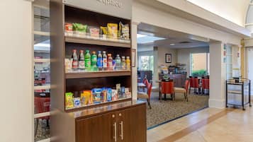 Un vestíbulo de hotel con zona de kitchenette, un letrero que indica kitchenette y un comedor con mesas y sillas.