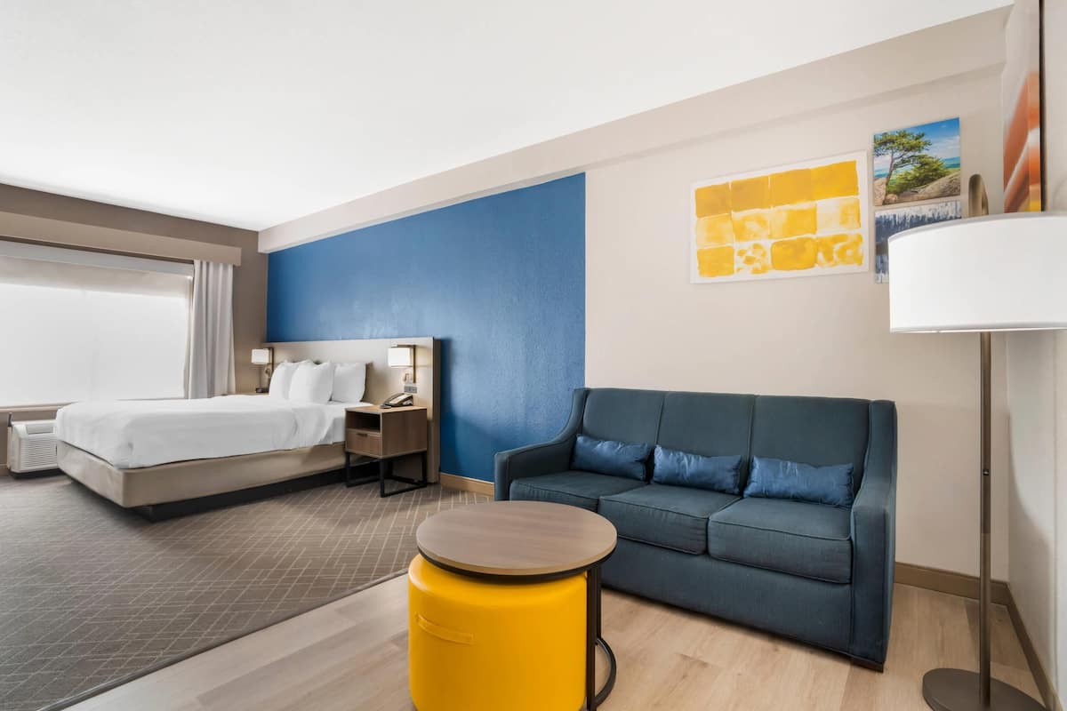 Une chambre d’hôtel avec un lit, un canapé, une petite table ronde et une lampe.