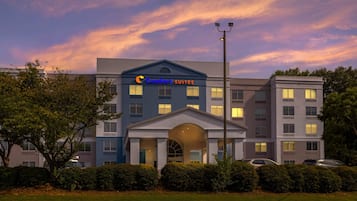 Un hotel con fachada moderna, un cartel llamativo que dice 'Comfort Suites' y un área de entrada bien cuidada.