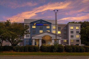 Un hotel con fachada moderna, un cartel llamativo que dice 'Comfort Suites' y un área de entrada bien cuidada.