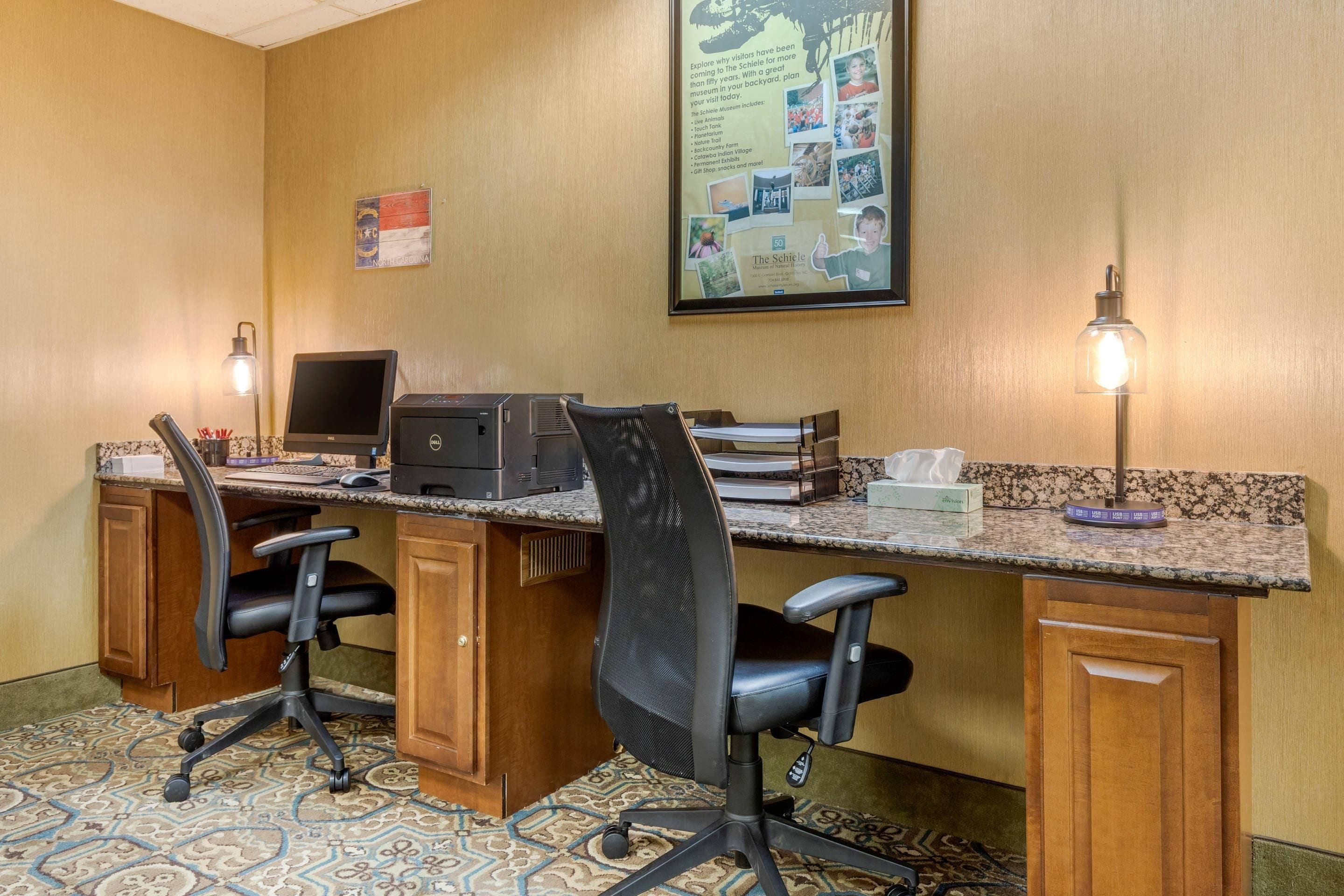 A conference room with a long table, two office chairs, a laptop, a printer, and a bulletin board.