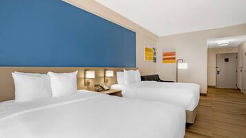 A hotel room with two beds, a blue accent wall, a bedside table with a lamp, and a door leading to another room.