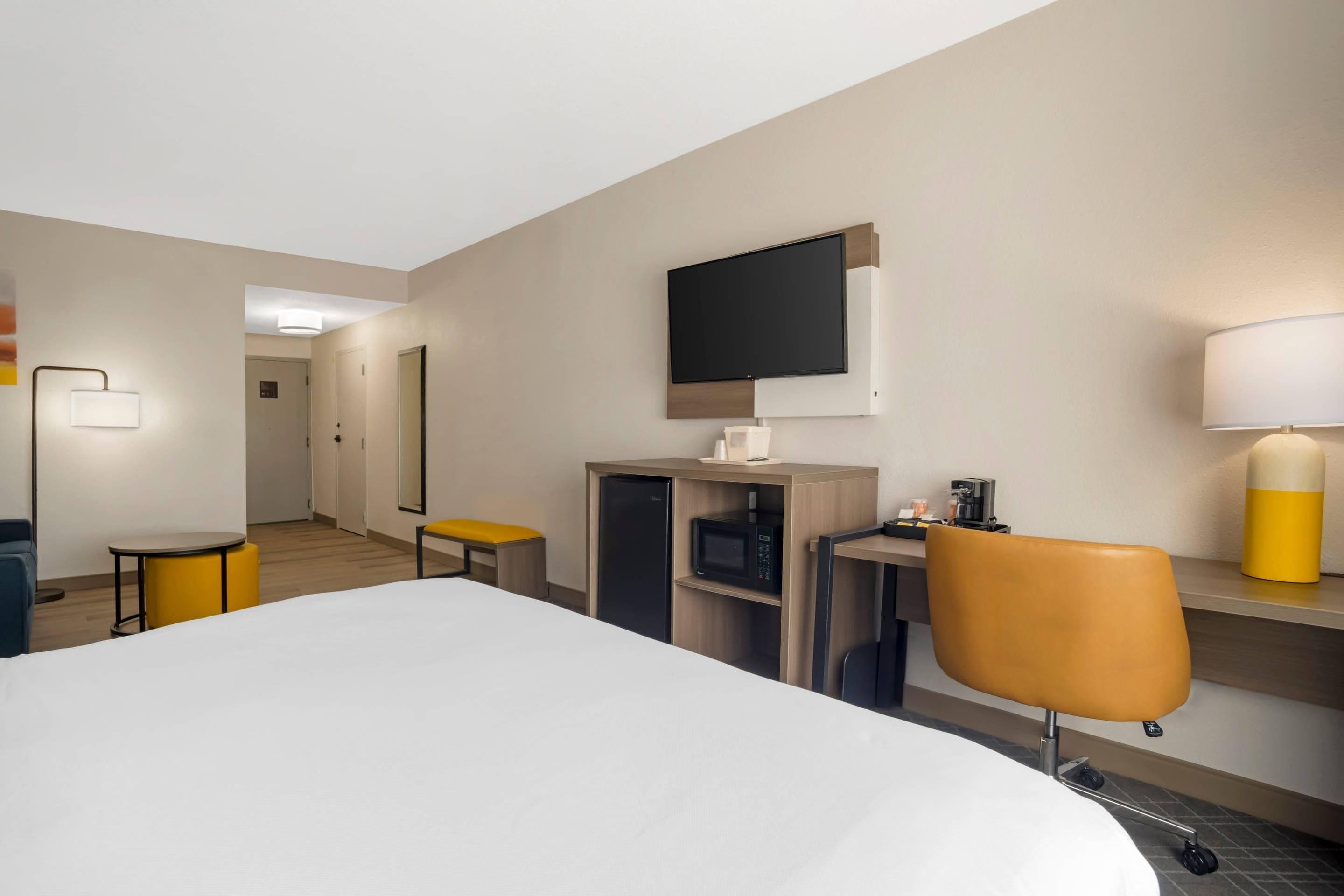 A hotel room with a bed, a desk with a chair, a television, a lamp, and a microwave.
