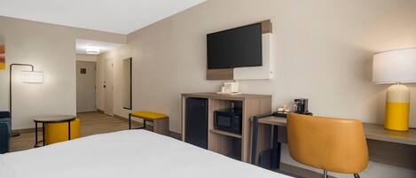 A hotel room with a bed, a desk with a chair, a television, a lamp, and a microwave.