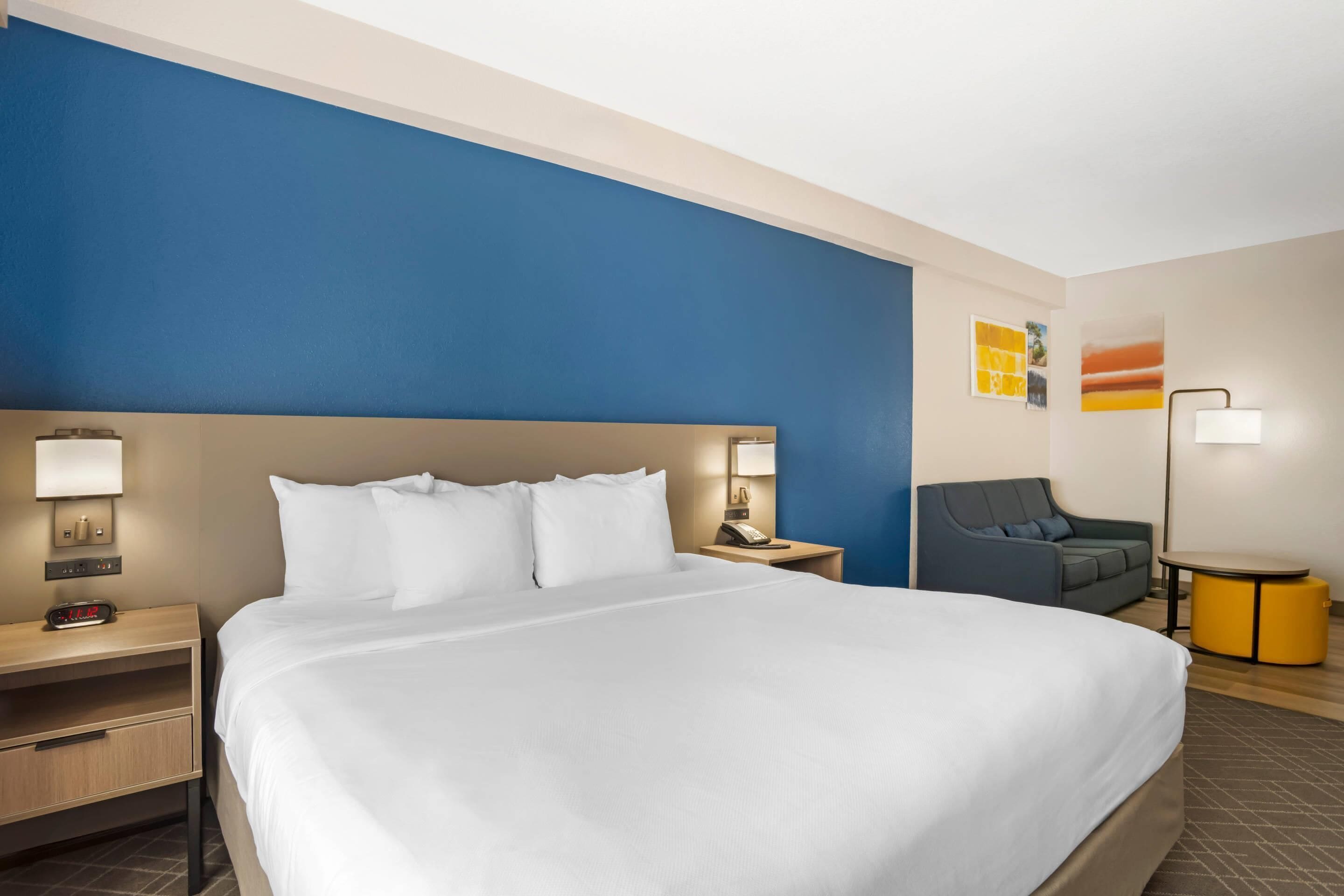 A hotel room with a large bed, bedside tables, a desk, a chair, and a lamp.